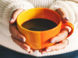Die Hände einer Frauen mit lackierten Fingernägeln halten eine Kaffeetasse.