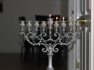 Ein Kerzenleuchter aus Silber mit zur Hälfte bestückten und noch brennenden Kerzen.