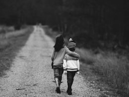 Ein schwarz-weiß Bild von zwei Kindern, die umarmt einen Waldweg entlang gehen.