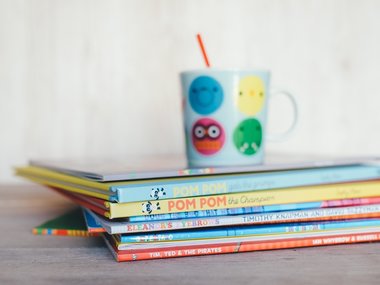 Ein Stapel bunter Kinderbücher mit einem bunten Becher oben auf.