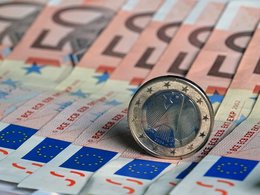 Kredit und Geld: Eine 1-Euro Münze rollt über eine Reihe 50-Euro Scheine.