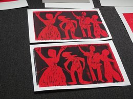 Zwei Kunstdrucke mit roten Figuren auf schwarzem Hintergrund liegt auf einem dunkelgrauen Teppich.
