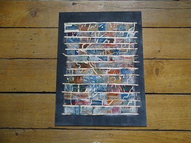 Eine Kunstdruck mit weißen Linien und bunten, gedeckten Farben, liegt auf einem Holzfußboden.