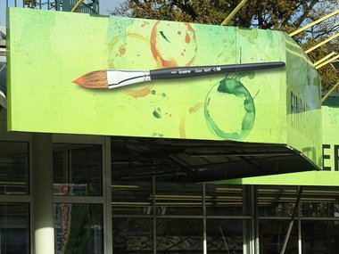Das Banner eines Gebäudes in hellgrün mit einem Pinsel und einigen Farbspritzern.