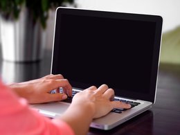 Zwei Hände schreiben auf der Tastatur eines Laptops.