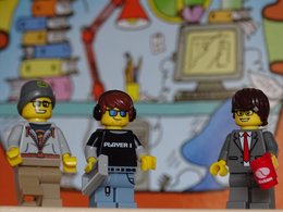 Drei Legomännchen mit einem Büro im Hintergrund.