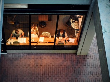 Der Einblick in ein Lokal, indem Personen am Fenster sitzen und lesen oder am Computer arbeiten.
