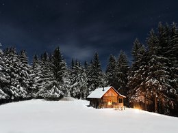 Lichtstrahlen fallen aus einem Fenster einer Hütte im verschneiten Wald.
