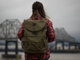 Der Rücken eines Mädchens mit einem Rucksack auf den Schultern und einer verschwommenen Brücke im Hintergrund.