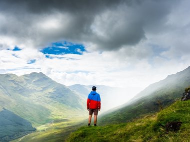 Ein Mann auf einer Anhöhe genießt die Aussicht ins Tal.
