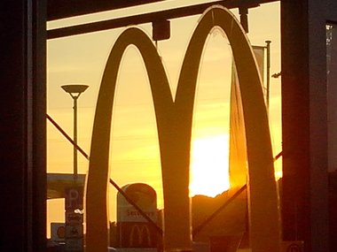 Das Werbe-Logo von McDonalds am Fenster eines Imbiss bei Sonnenuntergang.