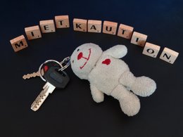 Aus Buchstabenplättchen ist das Wort Mietkaution aufgestellt worden und davor liegt ein Schlüsselbund mit einem Teddy.
