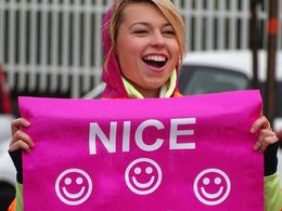 Eine junge Frau hält lachend ein pinkes Plakat in die Höhe auf dem mit weißer Schrift steht: nice legs.