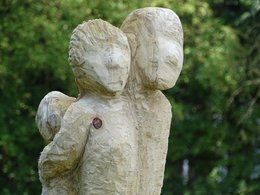 Ein Kunstwerk aus Holz von einer Frau, einem Mann und einem Kind auf dem Rücken.
