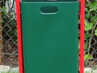 Eine grüne Mülltonne mit roten Halterung auf einer Wiese.