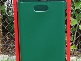 Eine grüne Mülltonne mit roten Halterung auf einer Wiese.