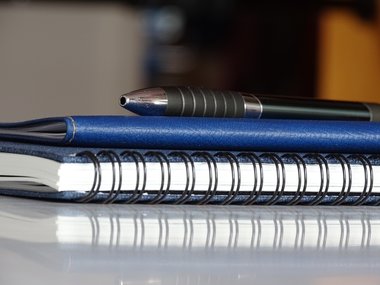 Notizblock, Terminkalender und Kugelschreiber auf einem Tisch.