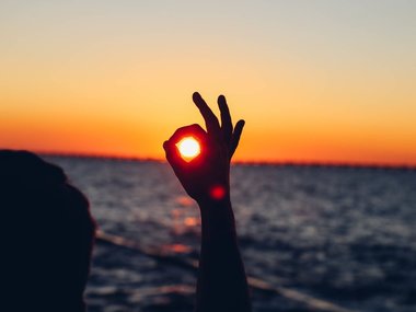 Eine Hand umkreist mit den Fingern die untergehende Sonne.