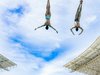 Zwei Sportlerinnen im Badeanzug bei einem Salto in der Luft.