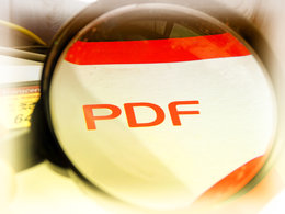 Eine Lupe vergrößert das Wort "PDF" in roter Schrift auf weißem Hintergrund.