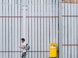 Ein Mann geht an einer Wand mit einem gelben Postkasten vorbei.