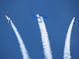 Vier Flugzeuge mit Red Bull-Werbung fliegen Kunststücke am blauen Himmel mit großen, weißen Kondenzstreifen.