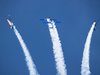 Vier Flugzeuge mit Red Bull-Werbung fliegen Kunststücke am blauen Himmel mit großen, weißen Kondenzstreifen.