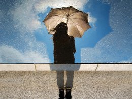 Eine Person mit Regenschirm spiegelt sich im Wasser.