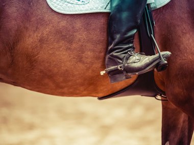 Die Beine eines Reiters auf einem Pferd mit Stiefel und Sporen.