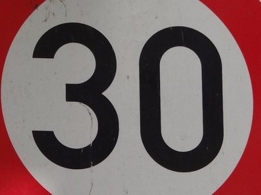 Ein Schild mit der schwarzen Aufschrift Zone 30 und von einem roten Kreis umrahmt.