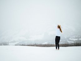 Eine Frau mit Zopf steht im Schnee und richtet sich die Haare.