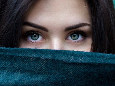 Die Augen einer Frau, die ihren Mund hinter einem Tuch versteckt.