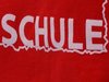 Der Rücken eines roten Shirtes mit der weißen Aufschrift: Schule und Handball-Camp.de.