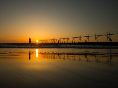 Ein Sonnenuntergang über dem Meer mit Brücke und einem Leuchtturm.