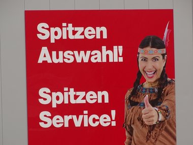 Ein rotes Schild mit einer Frau, die als Indianerin angezogen ist und der weißen Aufschrift: Spitzen Auswahl! Spitzen Service!