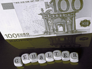 StepStone-Gehaltsreport: Buchstabenwürfel ergeben das Wort: Gehälter, welches sich auf einer glatten, roten Oberfläche widerspiegelt. Im Hintergrund ist ein 100 Eurogeldschein.