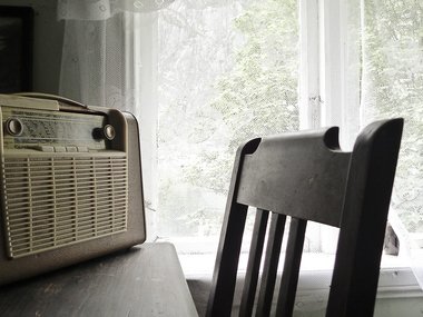 Ein Stuhl an einem Tisch mit einem alten Radio und einer Häkelgardine.