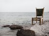 Ein Stuhl, der zum Teil im Meer, zum Teil in Muscheln steht.