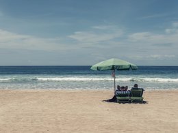 Ein Paar mit Liegestühlen und Sonnenschirm am menschenleeren Strand.