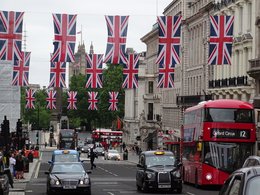 Straße in London, über die britische Nationalflaggen hängen und auf der ein typischer roter London-Bus entlang fährt.