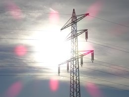 Ein Strommasten vor blauem Himmel mit Gegenlicht von der Sonne.
