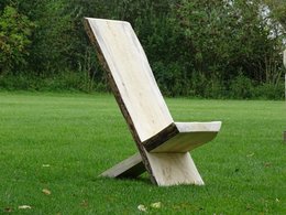 Ein großer, einfacher Holzstuhl auf einer grünen Wiese.