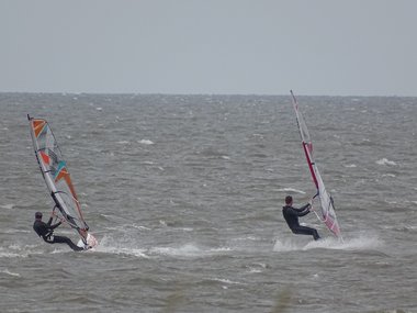 Zwei Surfer surfen in der grauen Nordsee.