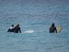 Drei Surfer warten mit ihrern Bretter auf eine Welle im Meer.