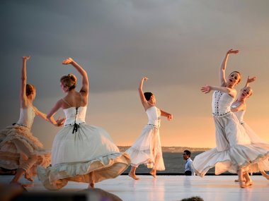 Tänzerinnen in weißen Kleidern auf einer Freiluftbühne.