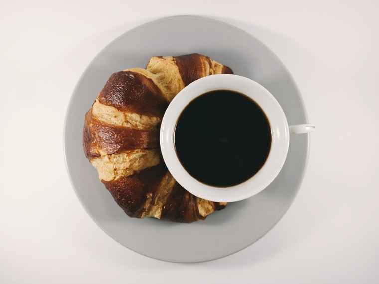 Eine Tasse-Kaffee und ein Croissant auf einem Teller.