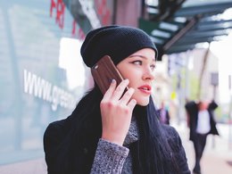 Telefoninterview - Eine geschminkte Frau mit schwarzer Mütze hält sich ein Handy ans Ohr.