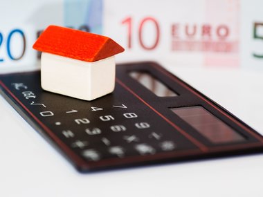 Ein kleines Haus auf einem Taschenrechner symbolisiert das Thema Umschuldung bei der Immobilienfinanzierung.