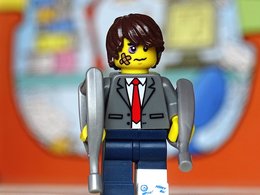 Ein Lego-Männchen im Anzug mit einem Gipsbein, Plaster und Verletzungen im Gesicht und Gehstützen..