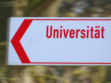 Der rote Schriftzug "Universität" auf einem weiße Schild weist den Weg zur Uni.